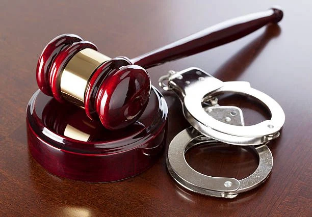A judge&rsquo;s gavel and a pair of handcuffs on a polished wooden desk